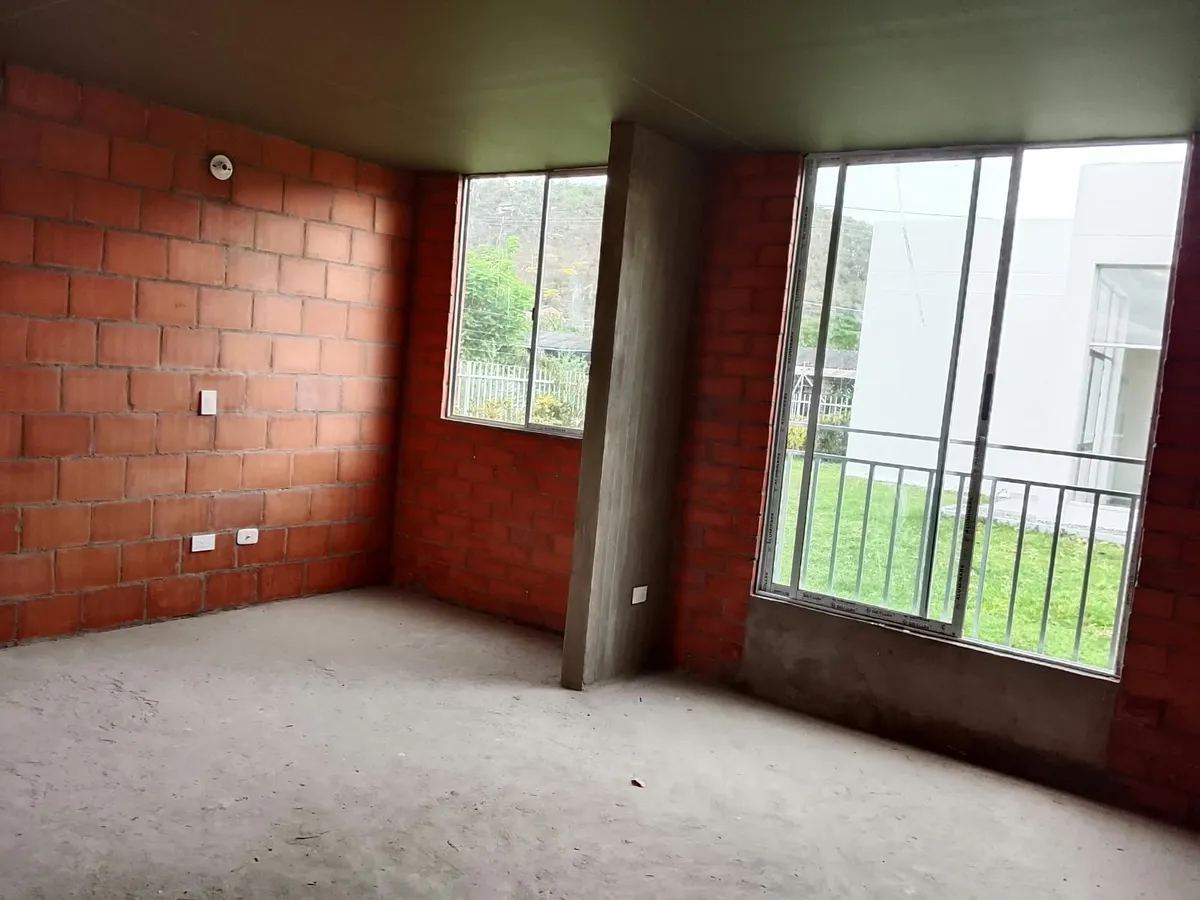 Sala comedor en obra gris con dos ventanales hacia la zona verde